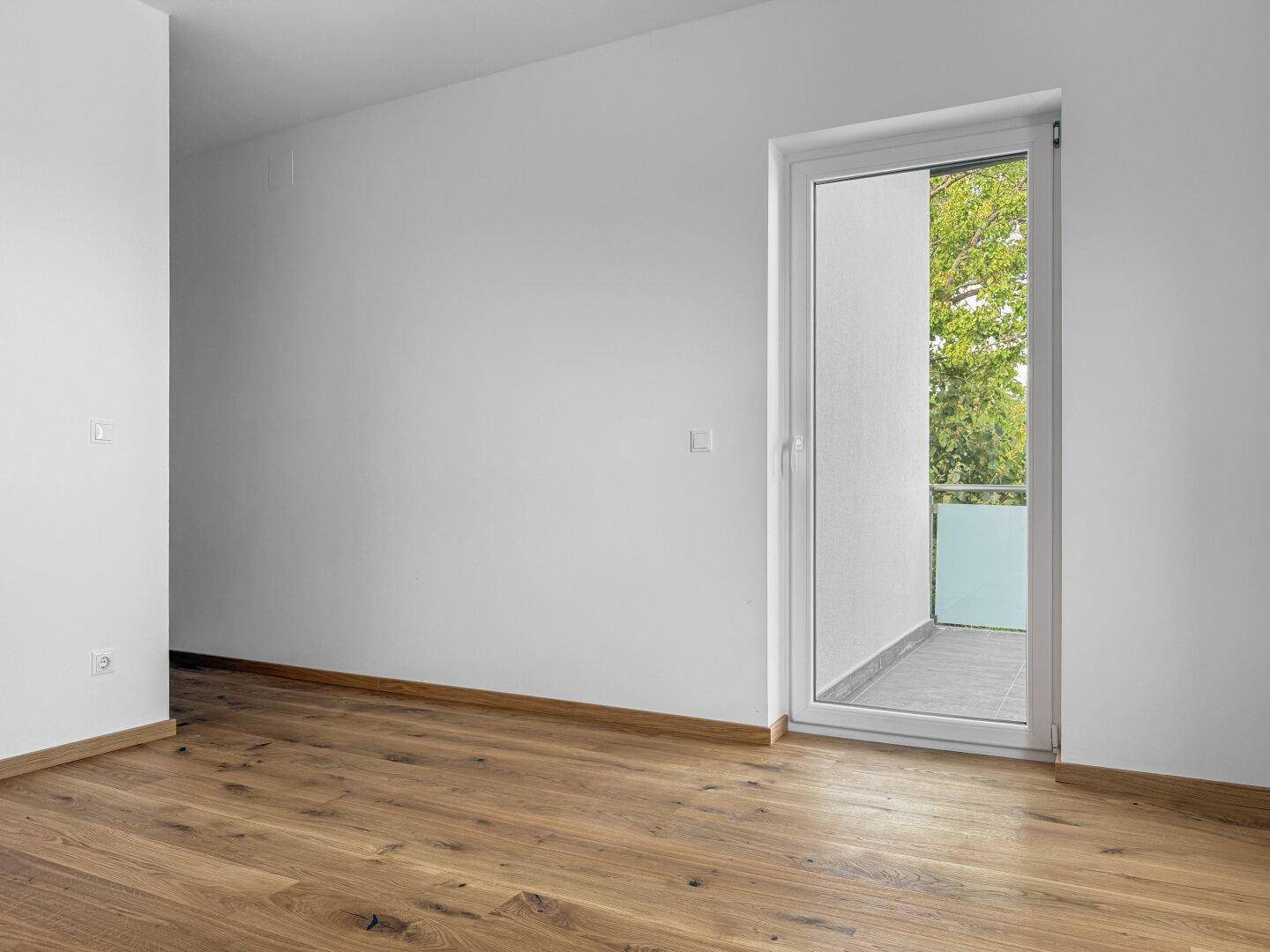 Geräumiges Zimmer mit Holzboden und direktem Zugang zu einem kleinen Balkon.