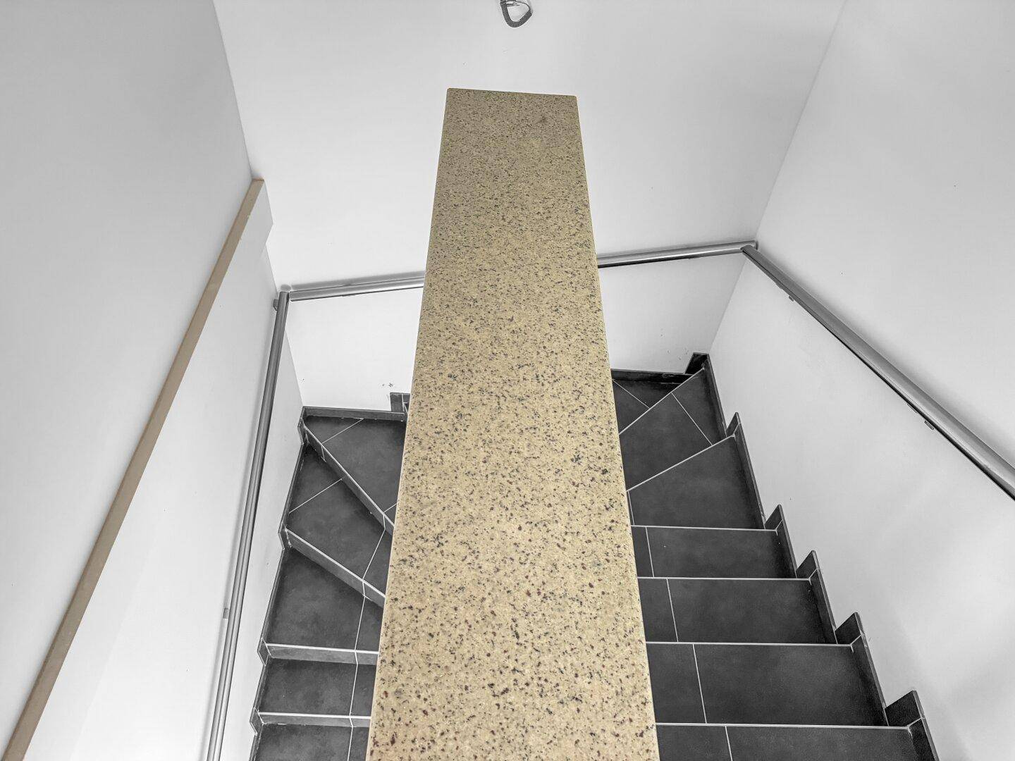 Moderne Treppe mit dunklen Fliesen und hellem Geländer, die die Stockwerke verbindet.