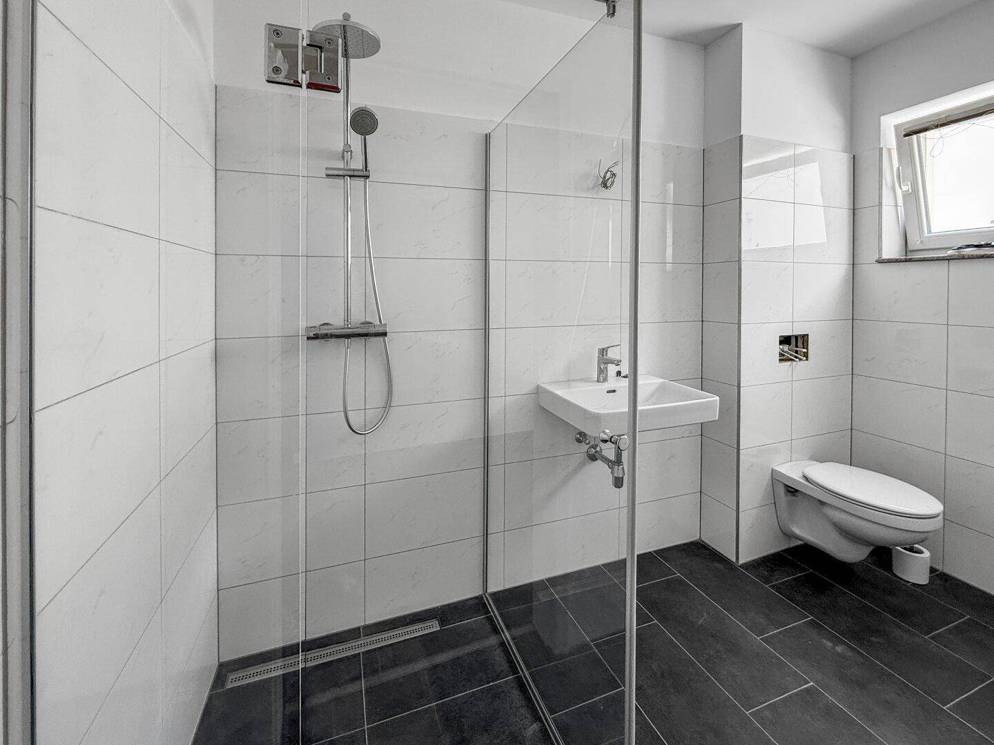 Modernes Badezimmer mit ebenerdiger Dusche, Wand-WC und dunklen Bodenfliesen.