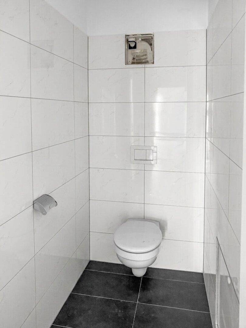 Separates WC mit Wandtoilette und weißen Fliesen, funktional und sauber.