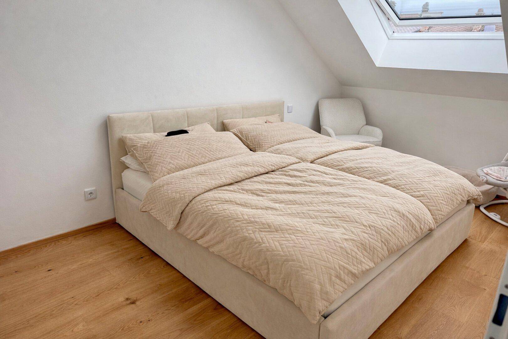 Helles Schlafzimmer im Dachgeschoss mit Doppelbett, Holzboden und großem Dachfenster.
