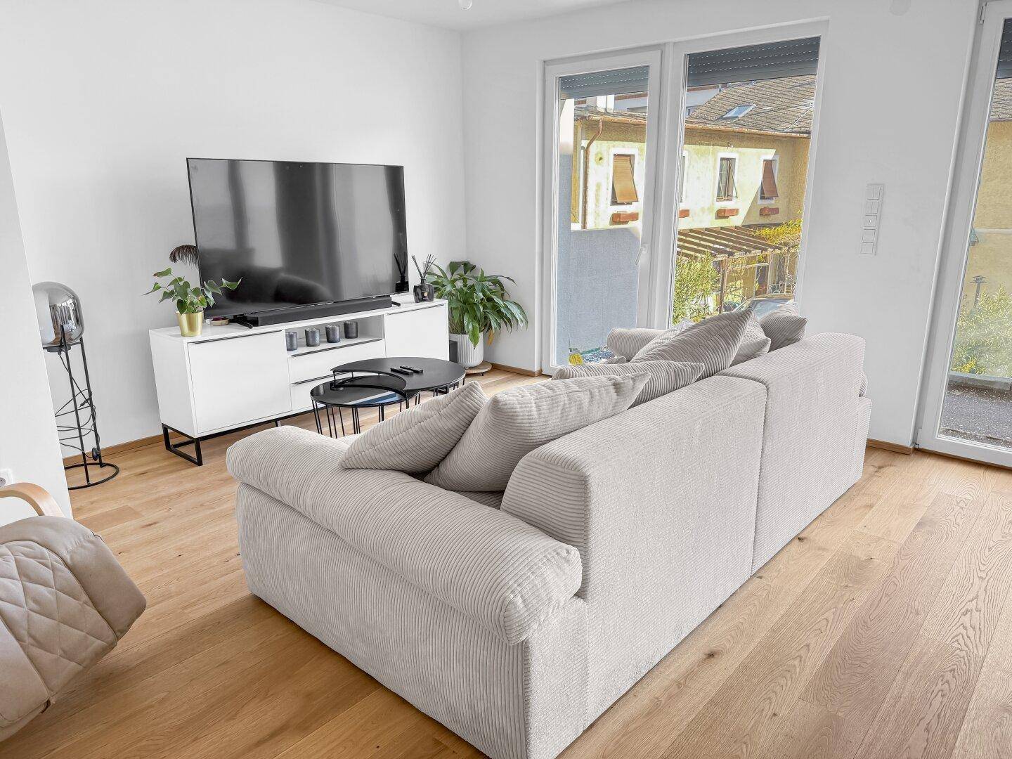 Gemütliches Wohnzimmer mit großem Sofa, Fernseher und Zugang zu einem Außenbereich.