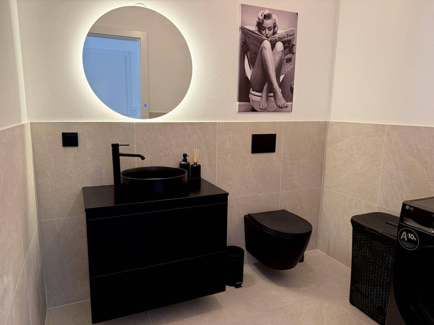 Modernes Gäste-WC mit schwarzem Waschbecken, Toilette und beleuchtetem Spiegel.