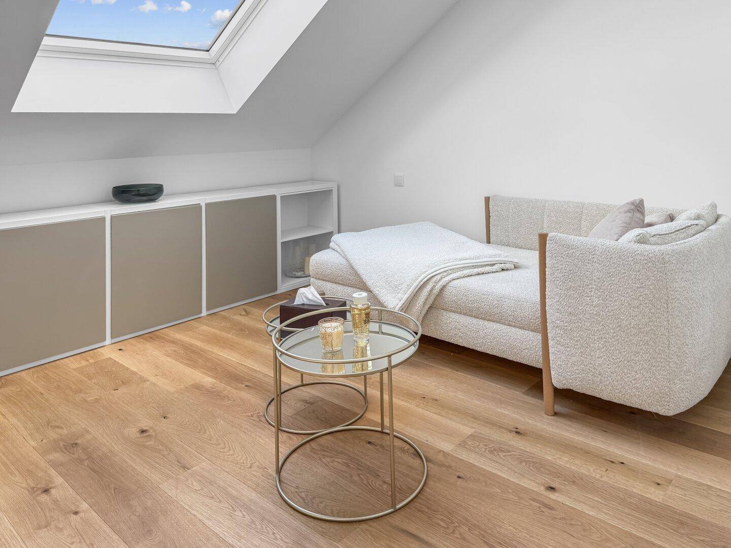 Gemütlicher Dachbodenraum mit Sofa, Holzboden und Dachfenster für natürliches Licht.