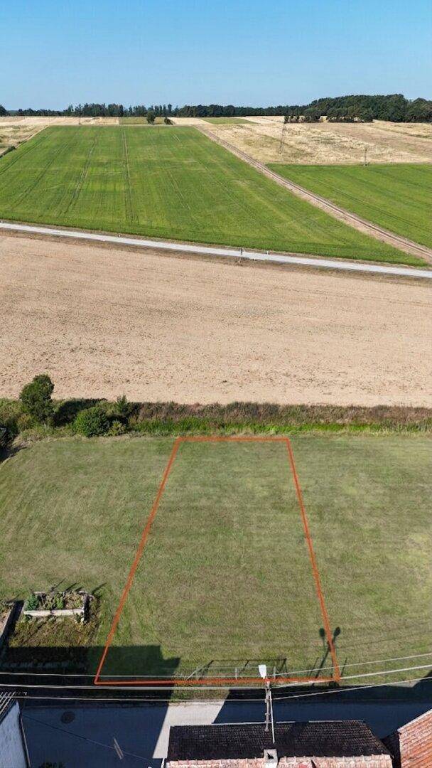 Luftaufnahme eines rechteckigen Grundstücks mit roter Markierung, umgeben von Feldern, Straße und Häusern.