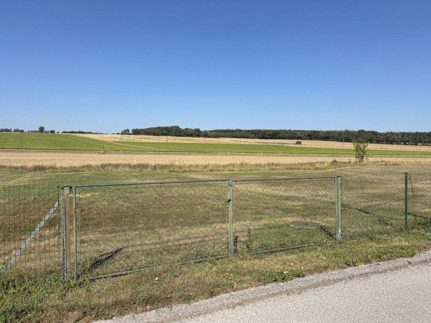 Weitläufiges Grundstück mit Zaun und Blick auf die umliegende Natur und Felder an einem sonnigen Tag.