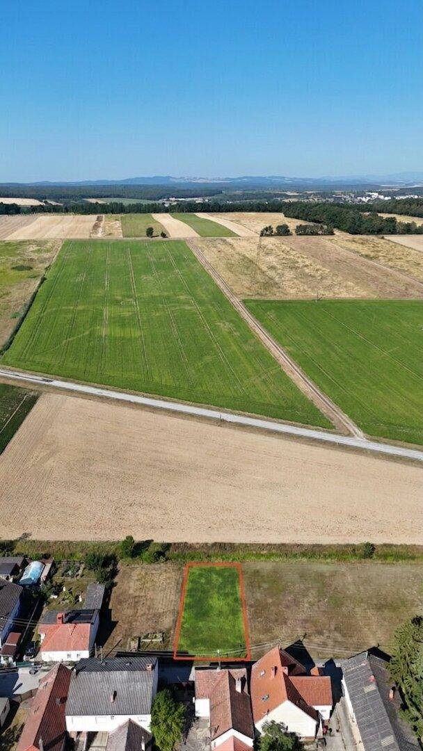 Weitwinkel-Luftaufnahme eines Grundstücks mit roter Umrandung, angrenzend an ein Dorf und weite Felder.