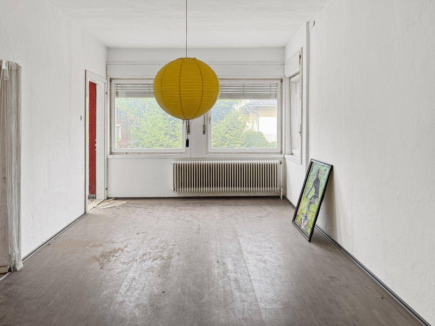 Heller Raum mit zwei Fenstern, Heizkörpern und Laminatboden, bereit zur individuellen Gestaltung.