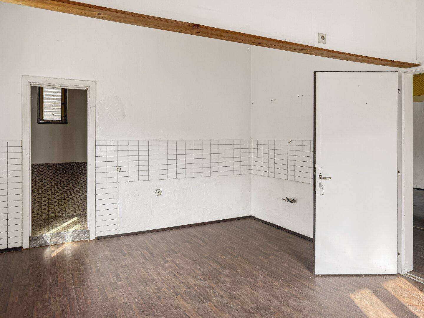 Leere Küche oder Hauswirtschaftsraum mit weißen Fliesenwänden, Holzbalken und dunklem Holzboden.