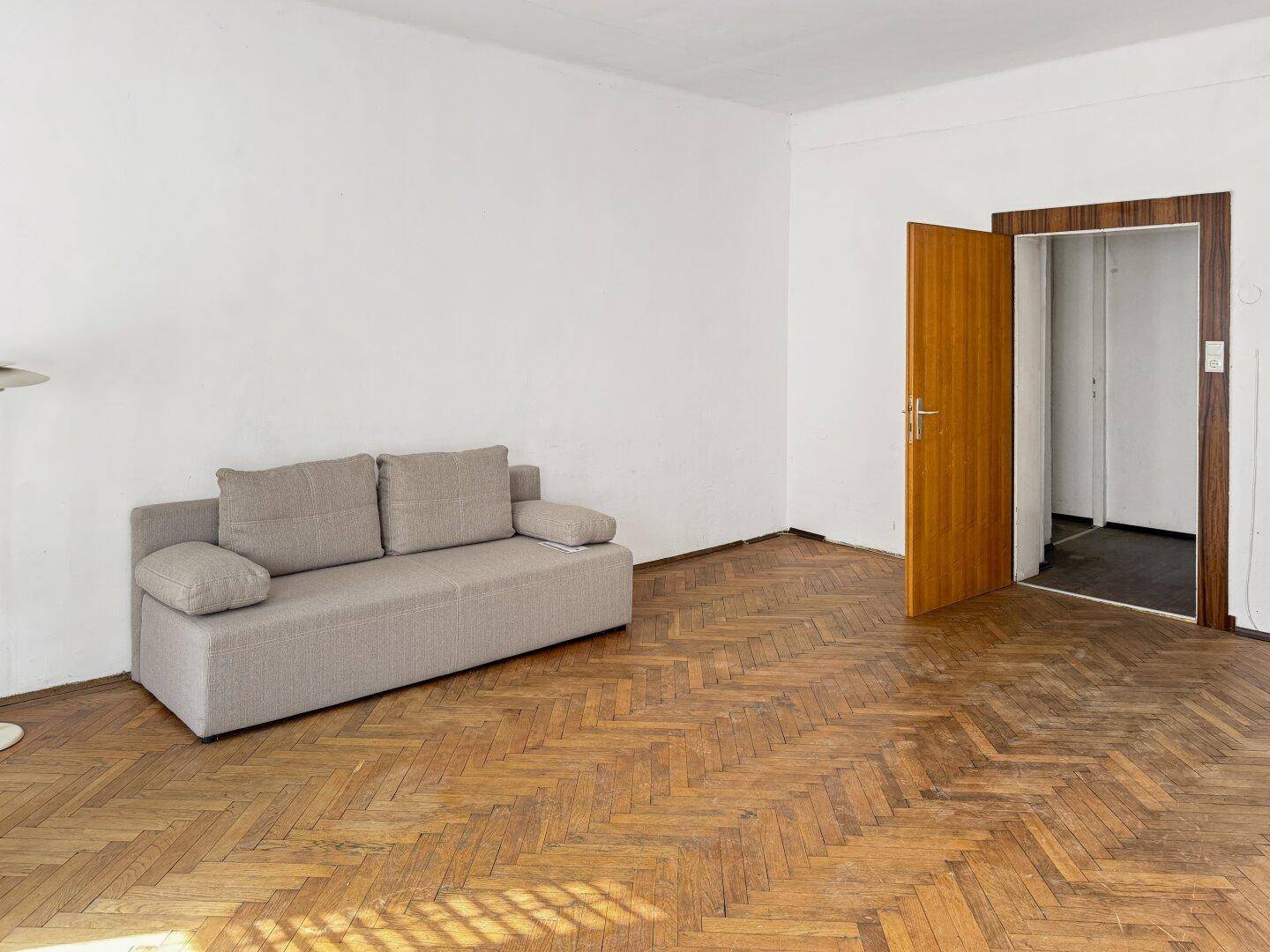 Gemütliches Wohnzimmer mit Fischgrätparkett, weißen Wänden und einem beigen Sofa.