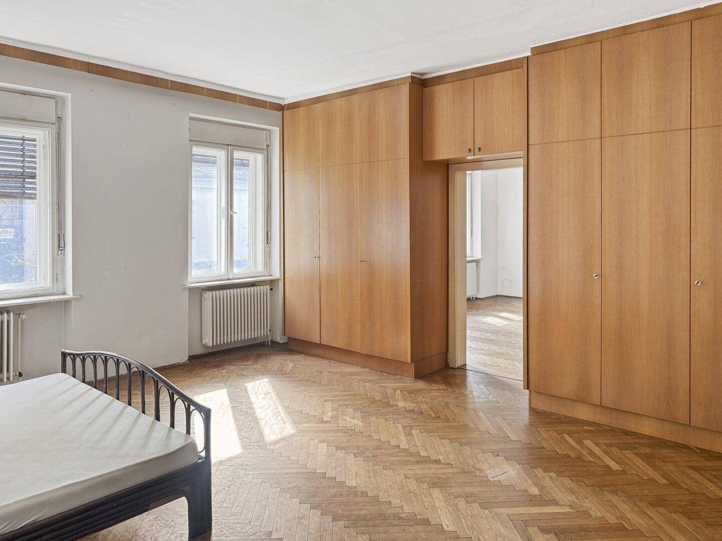 Schlafzimmer mit Fischgrätparkett, Einbauschränken aus Holz und einem Bettgestell.