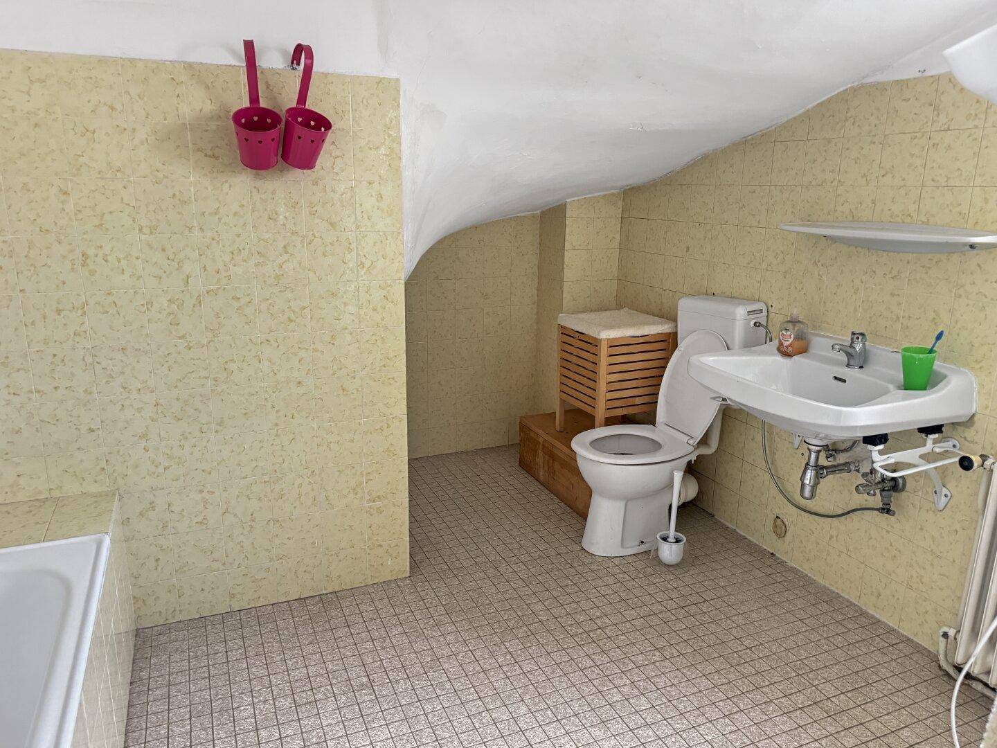 Badezimmer mit gelb gemusterten Fliesen, Toilette, Waschbecken und einer Dachschräge.