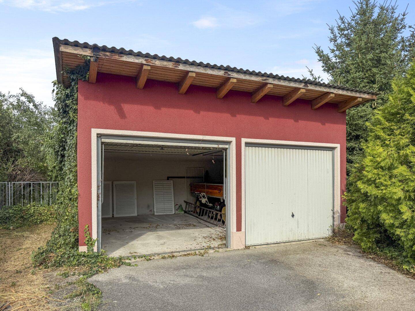 Doppelgarage mit einem offenen und einem geschlossenen Tor, umgeben von Grün.