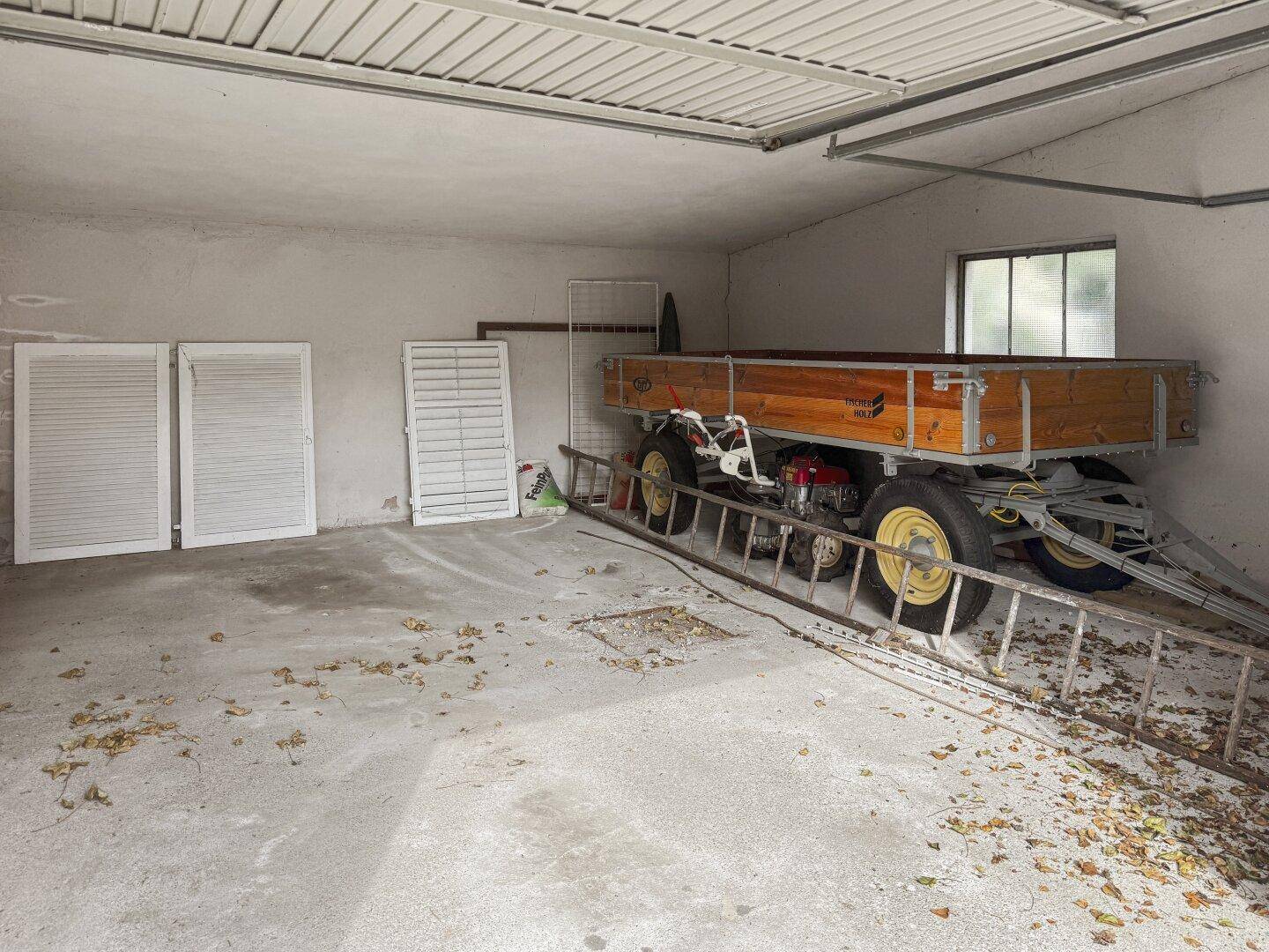Innenansicht der Garage mit Betonboden, Fenster und verschiedenen gelagerten Gegenständen.