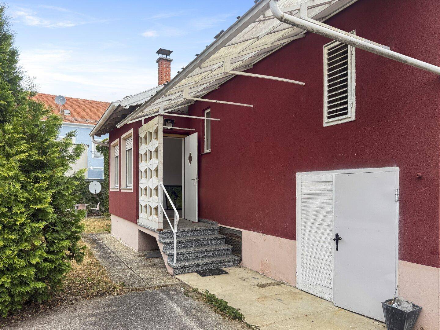 Seitlicher Eingang des Hauses mit Betontreppe und einem kleinen Nebengebäude daneben.