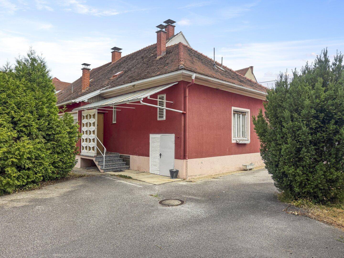 Rote Hausfassade mit Satteldach, Außentreppe und Zugang zum Kellerbereich.