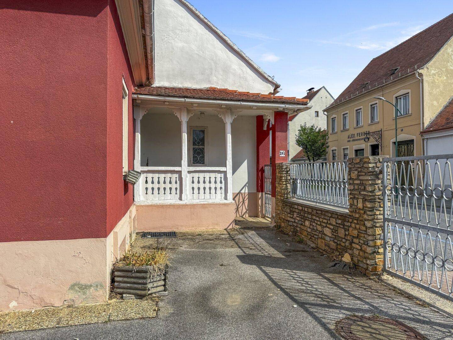Eingangsbereich mit überdachter Veranda, dekorativem Geländer und Steinmauer.
