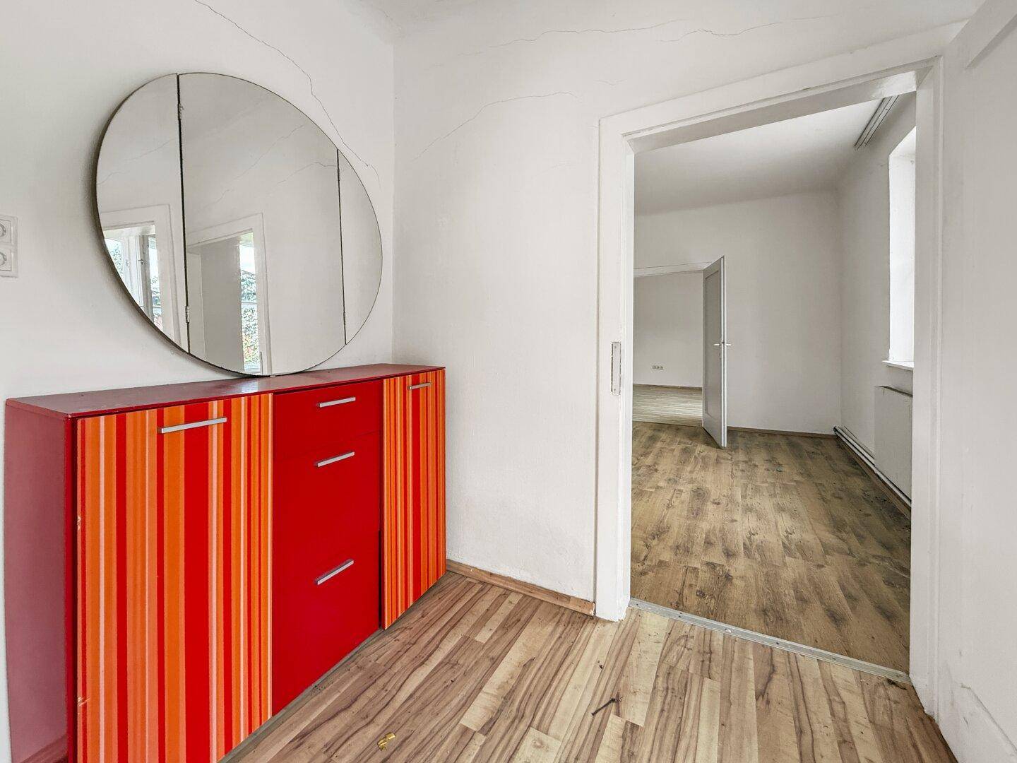 Heller Flur mit farbenfrohem Schrank, großem Spiegel und Blick in einen angrenzenden Raum.