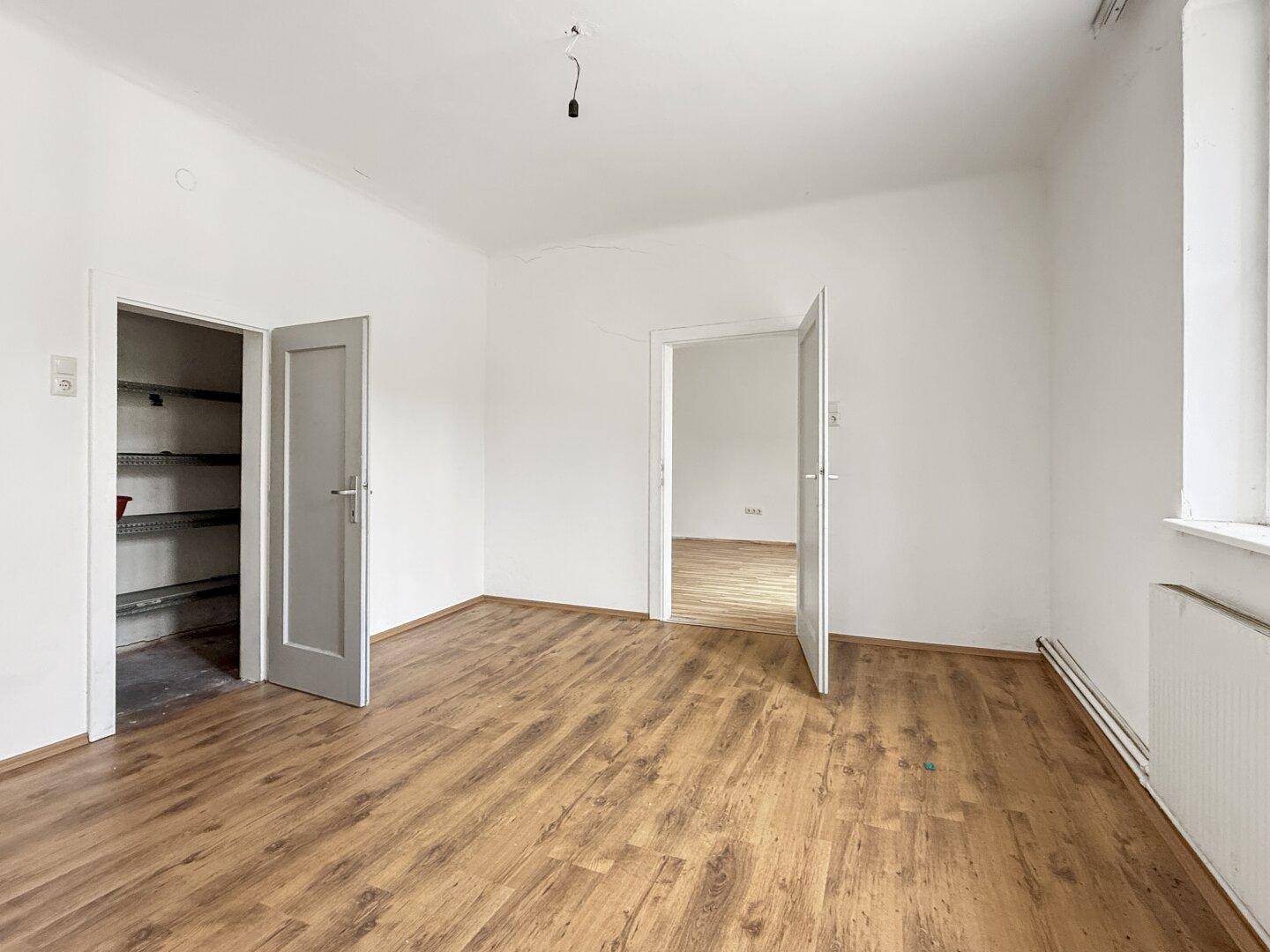 Helles, leeres Zimmer mit Laminatboden und Zugang zu einem Abstellraum und einem weiteren Raum.