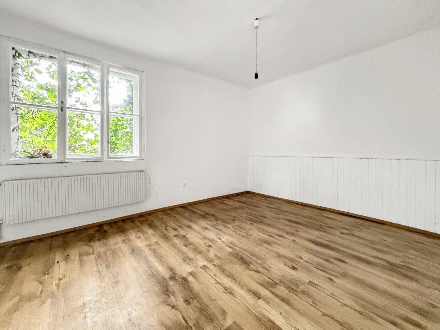 Geräumiges Zimmer mit Laminatboden, weißen Holzpaneelen an der Wand und großen Fenstern.