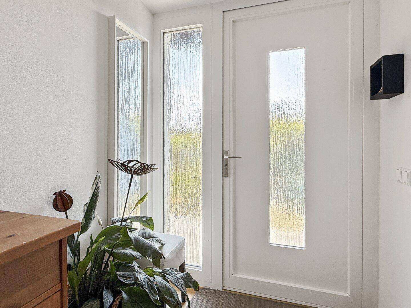 Eingangstür mit Glasausschnitten und seitlichen Fenstern, die viel Licht hereinlassen.