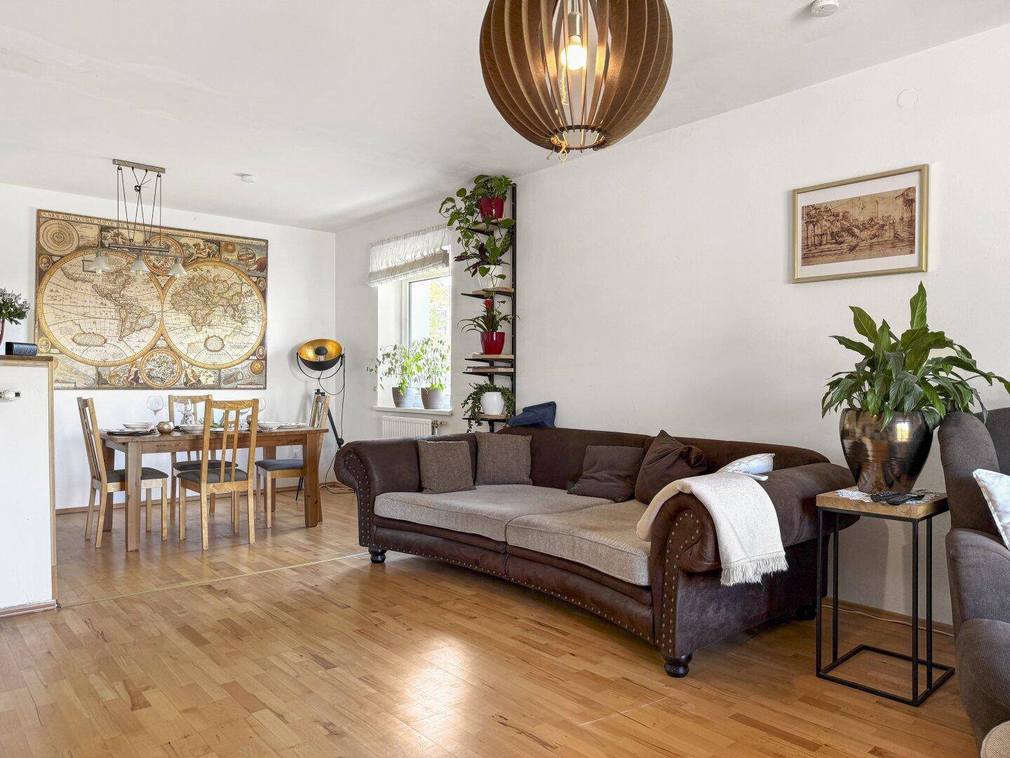 Geräumiger Wohn-Essbereich mit Holzboden, großem Sofa und dekorativer Weltkarte.