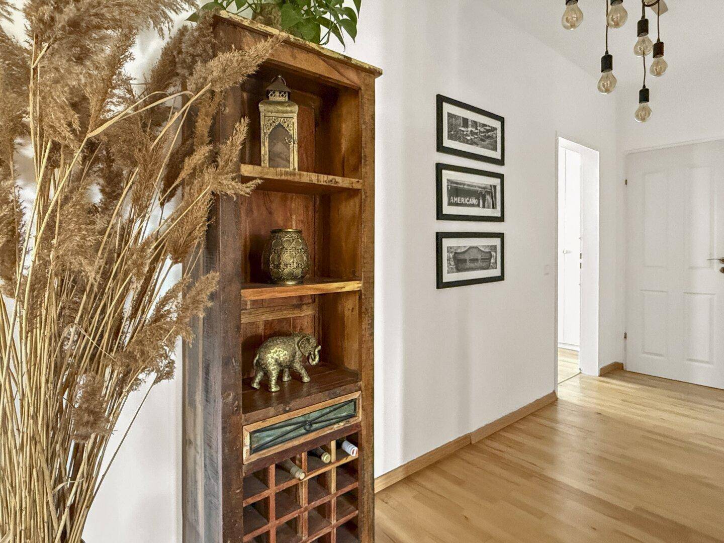 Dekorativer Holzschrank mit Weinfach und Trockenblumen in einem hellen Flur.