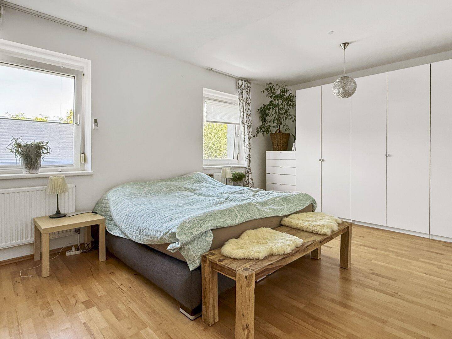 Geräumiges Schlafzimmer mit Holzboden, großem Bett und weißen Kleiderschränken.