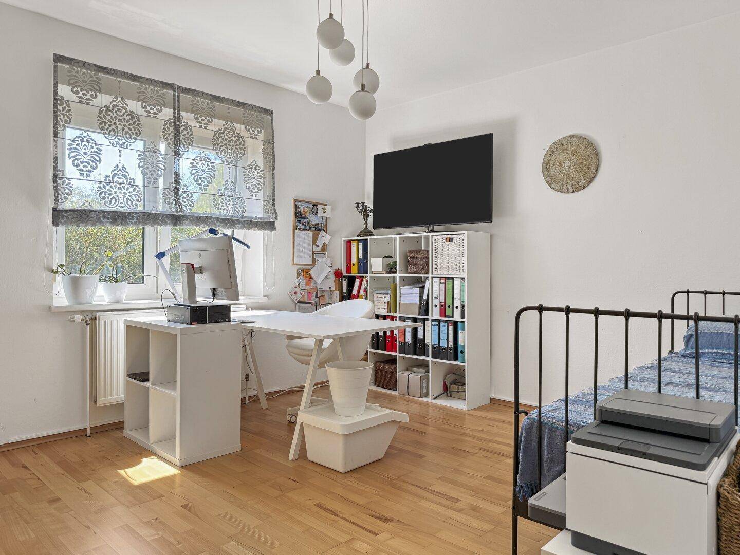 Helles Arbeitszimmer mit Schreibtisch, Regal und einem Bett, das auch als Gästezimmer dienen kann.