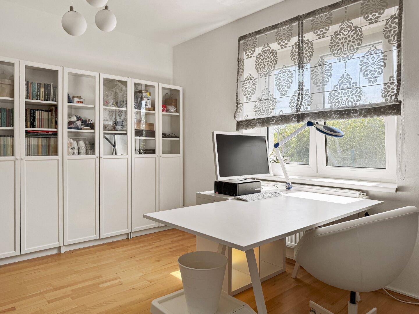 Arbeitszimmer mit großem Schreibtisch, Büchern in Vitrinen und Blick ins Grüne.