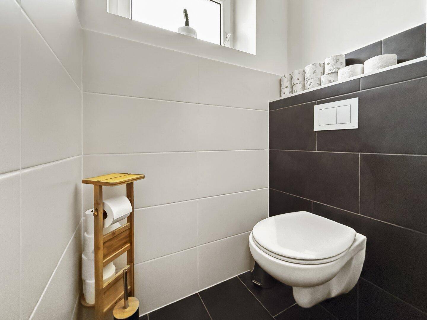 Modernes Gäste-WC mit Wand-WC, Fenster und zweifarbigen Fliesen in Weiß und Anthrazit.