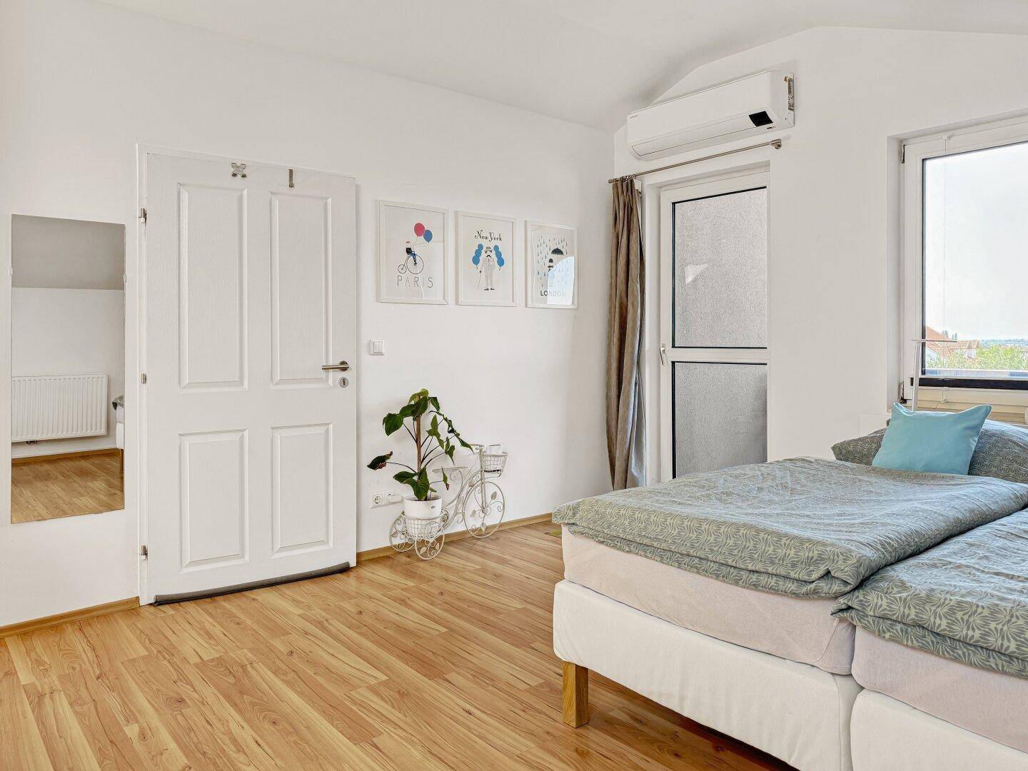 Helles Schlafzimmer mit zwei Einzelbetten, Holzboden, Klimaanlage und Zugang zum Balkon.