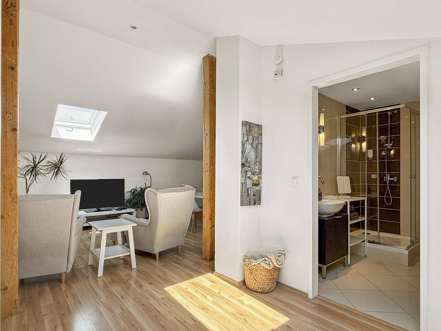 Offener Wohnbereich mit Fernseher, Sesseln und Blick auf ein modernes Badezimmer.
