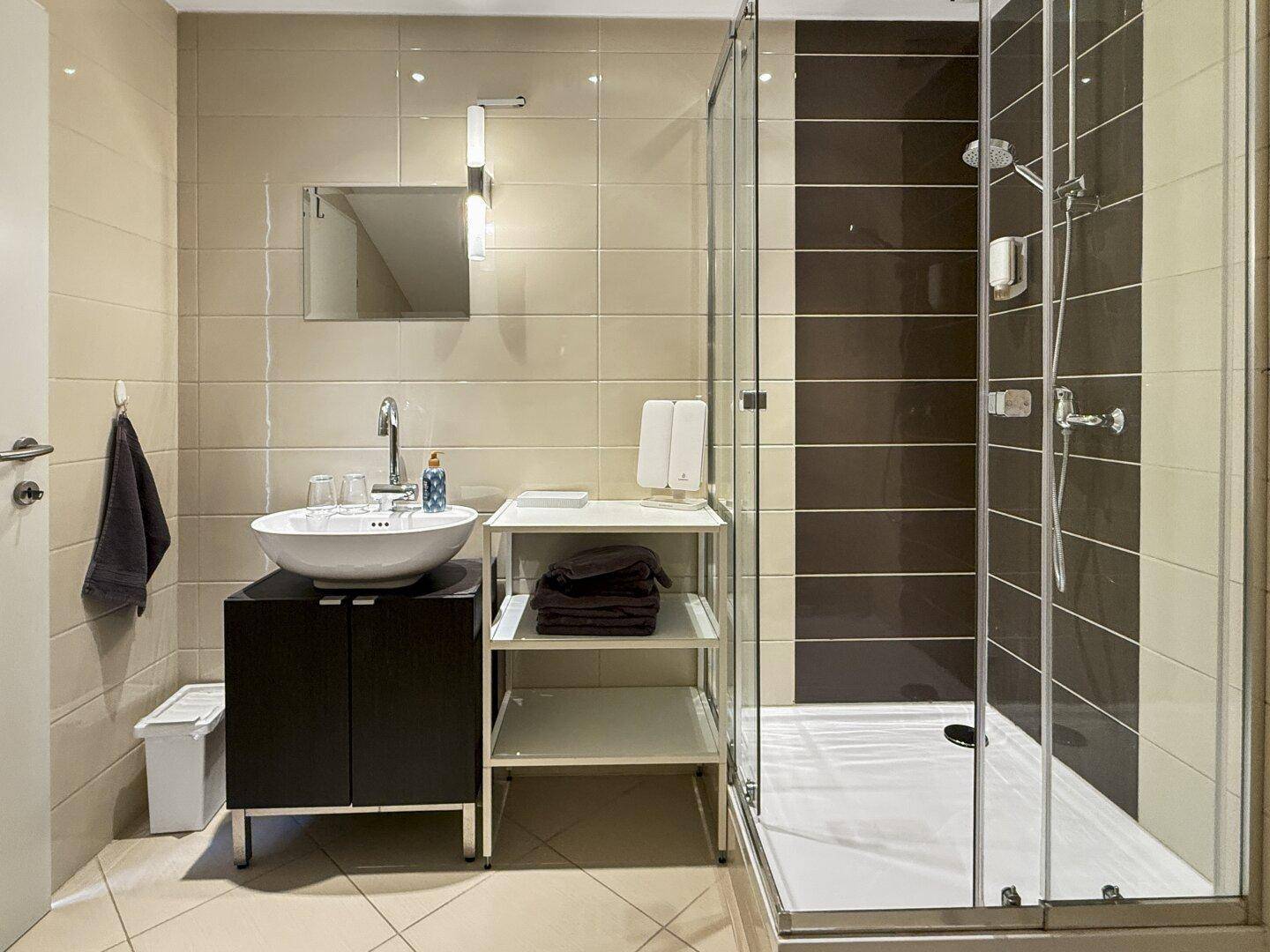 Modernes Badezimmer mit beigefarbenen Fliesen, Aufsatzwaschbecken und Glasduschkabine.