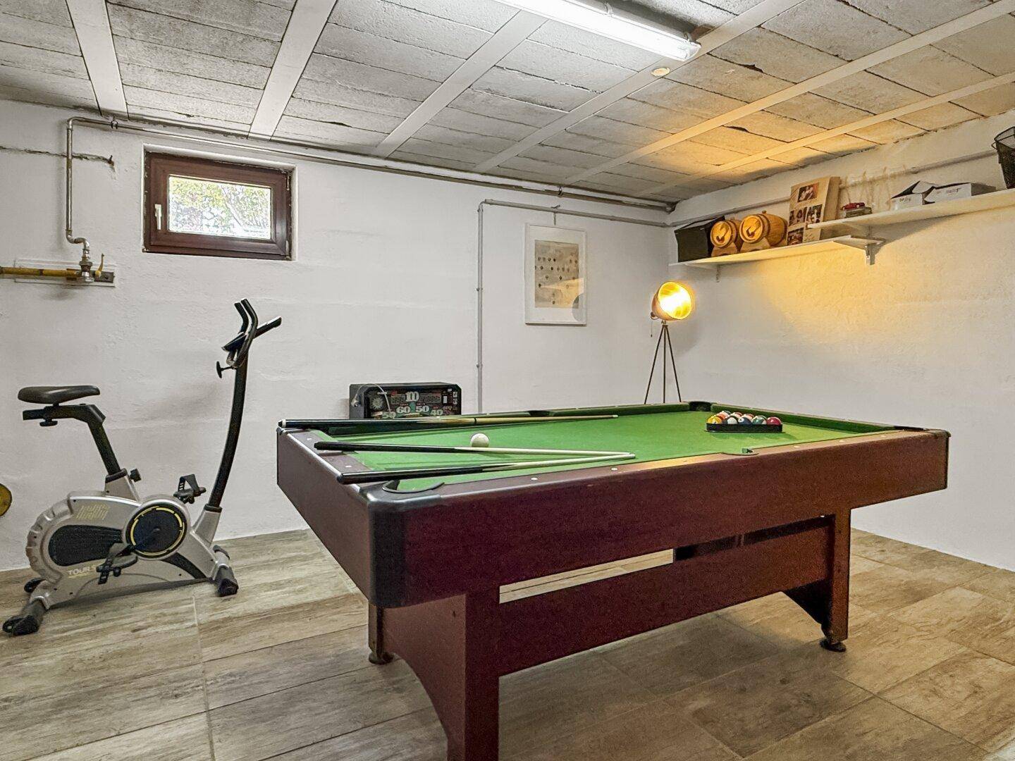 Untergeschossraum mit Billardtisch, Fitnessgerät und freiliegenden Rohren an der Decke.