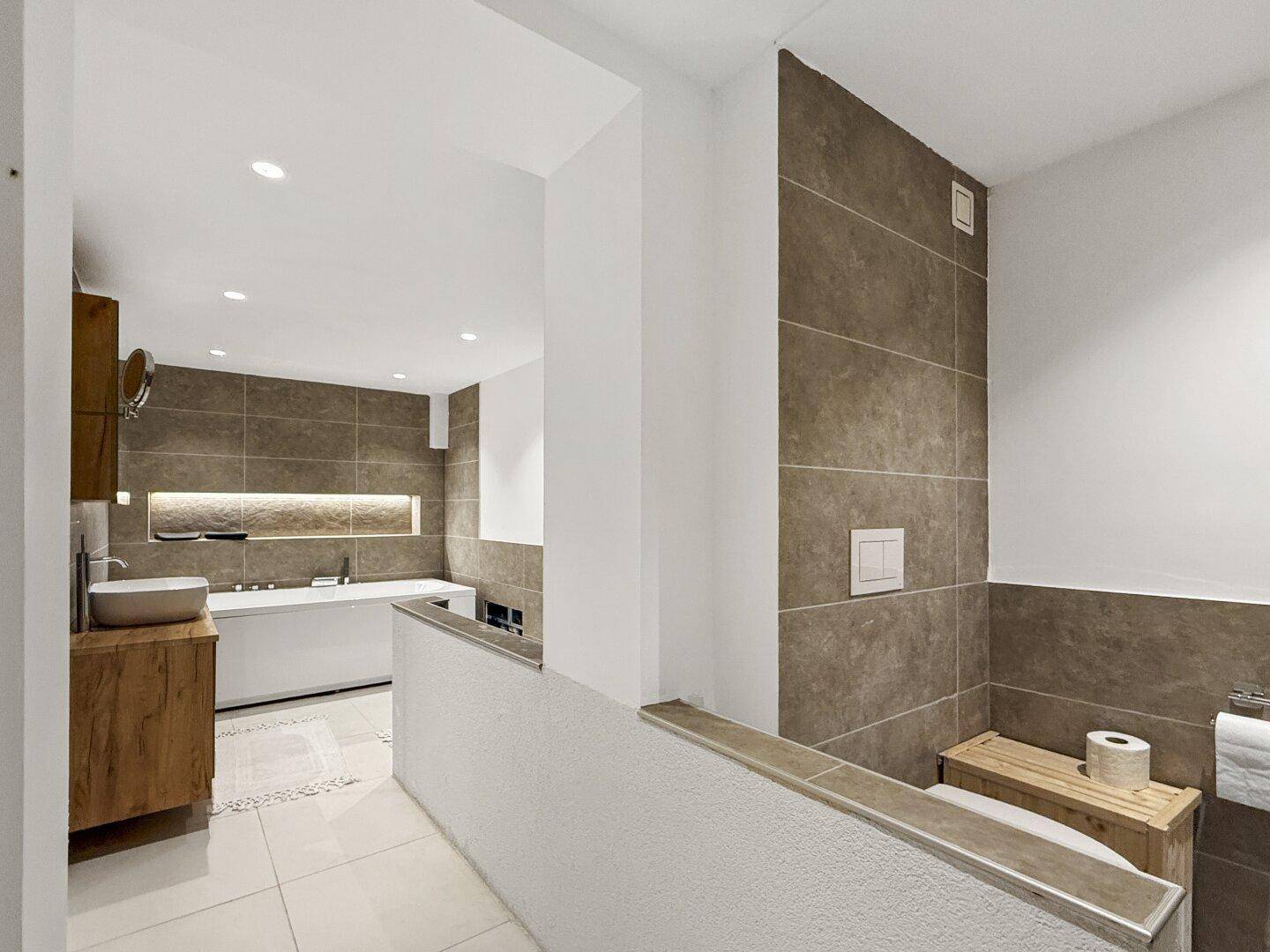 Modernes Badezimmer mit Badewanne, Holzwaschtisch und grauen Fliesen.