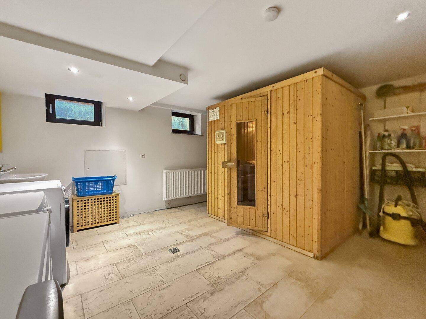 Geräumiger Wellnessbereich im Untergeschoss mit Sauna, Fenstern und Fliesenboden.
