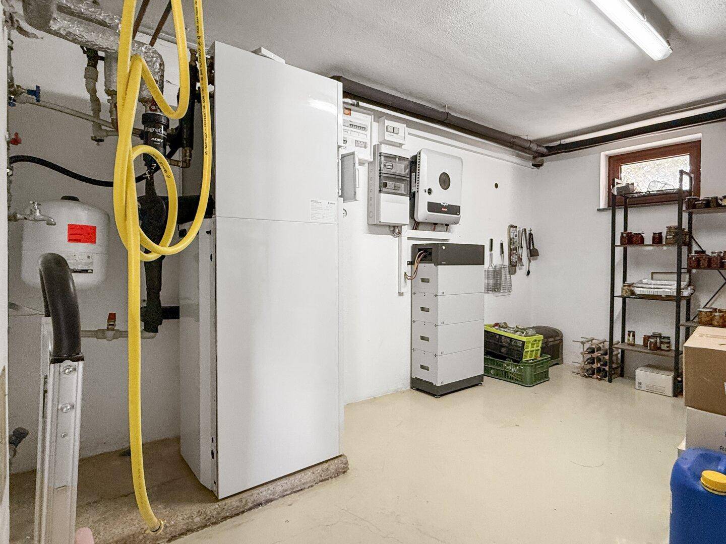 Technikraum im Keller mit Heizungsanlage, elektrischen Schaltkästen und Lagerregalen.