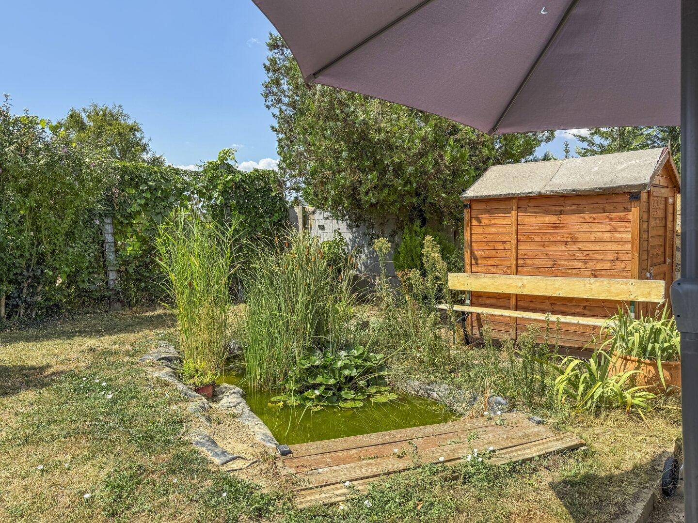 Idyllischer Gartenbereich mit kleinem Teich, Gartenhaus und üppiger Bepflanzung für Entspannung.