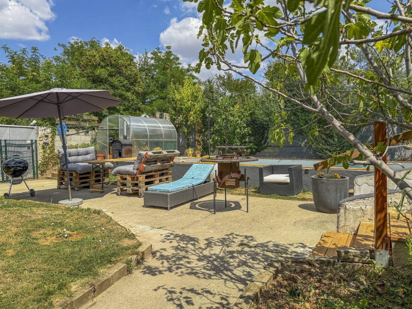 Gemütlicher Außenbereich mit Palettenmöbeln, Grill und Blick auf den Pool sowie das Gewächshaus.