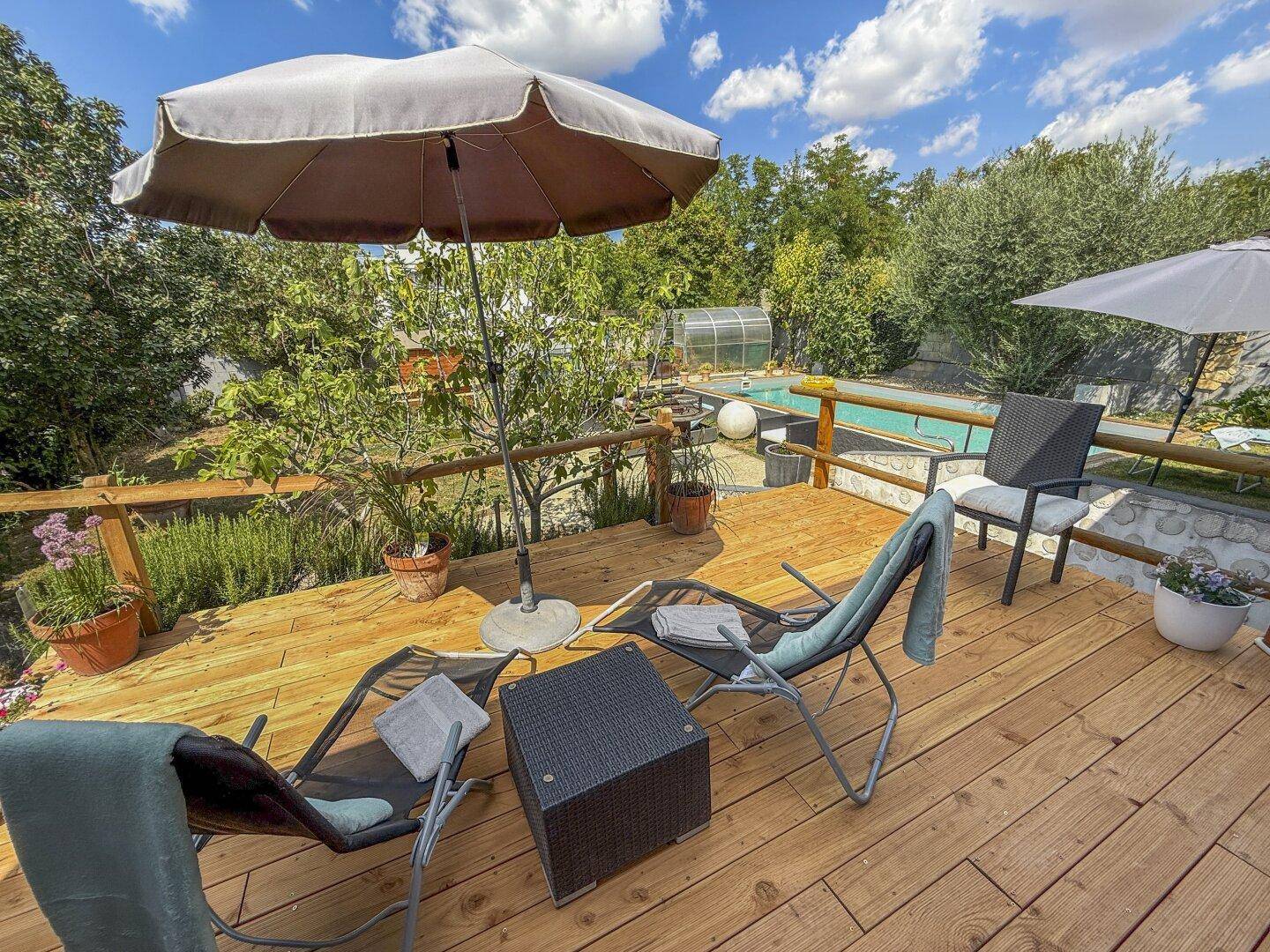 Geräumige Holzterrasse mit Blick auf den Garten und den Poolbereich, perfekt für gesellige Stunden.