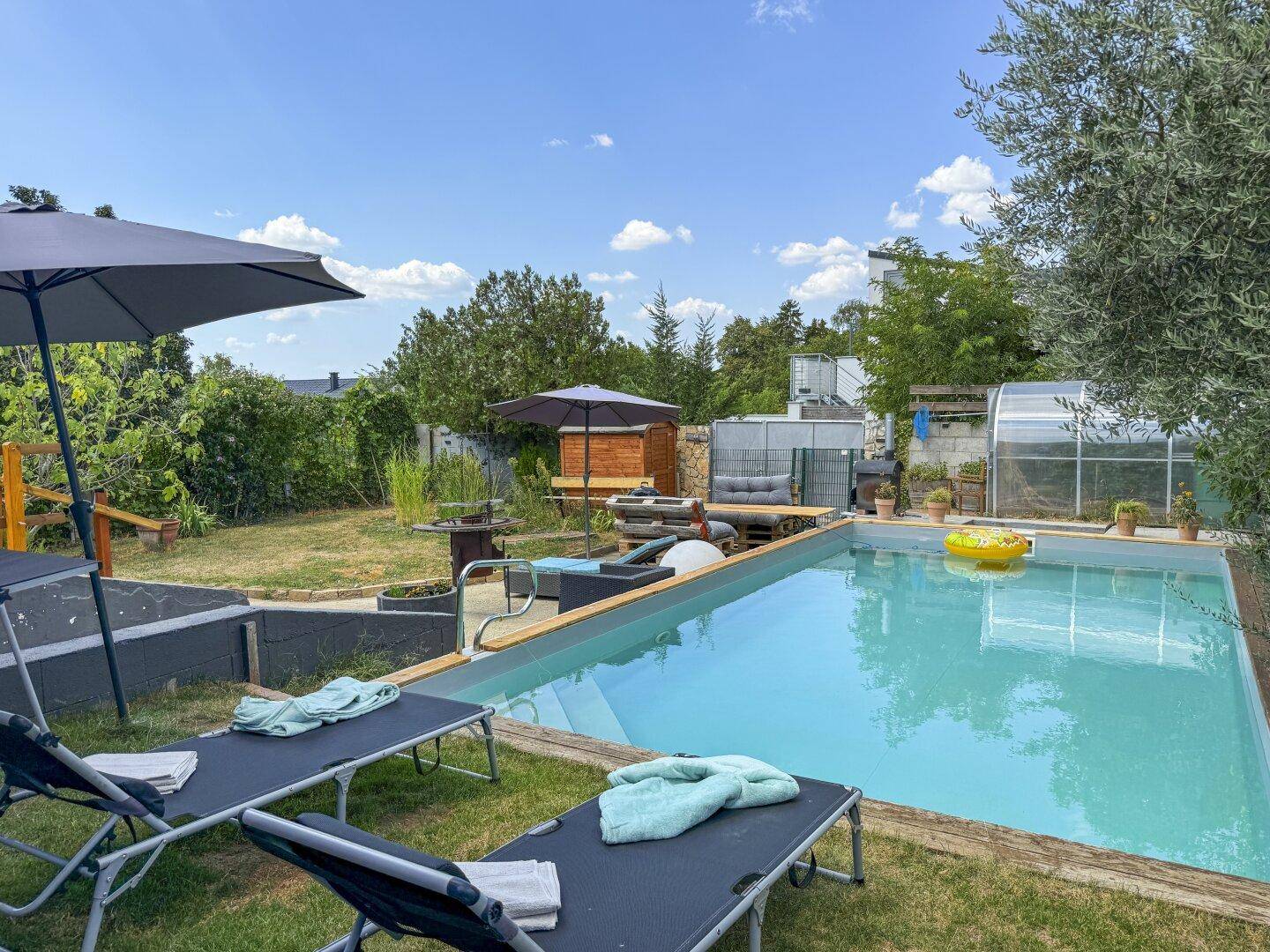 Sonnige Gartenoase mit erfrischendem Pool, bequemen Liegestühlen und üppiger Vegetation.
