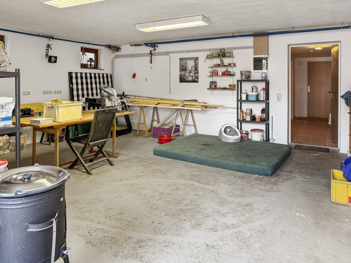 Geräumige Garage, die als Werkstatt genutzt wird, mit Arbeitsflächen, Werkzeugen und Lagerplatz.