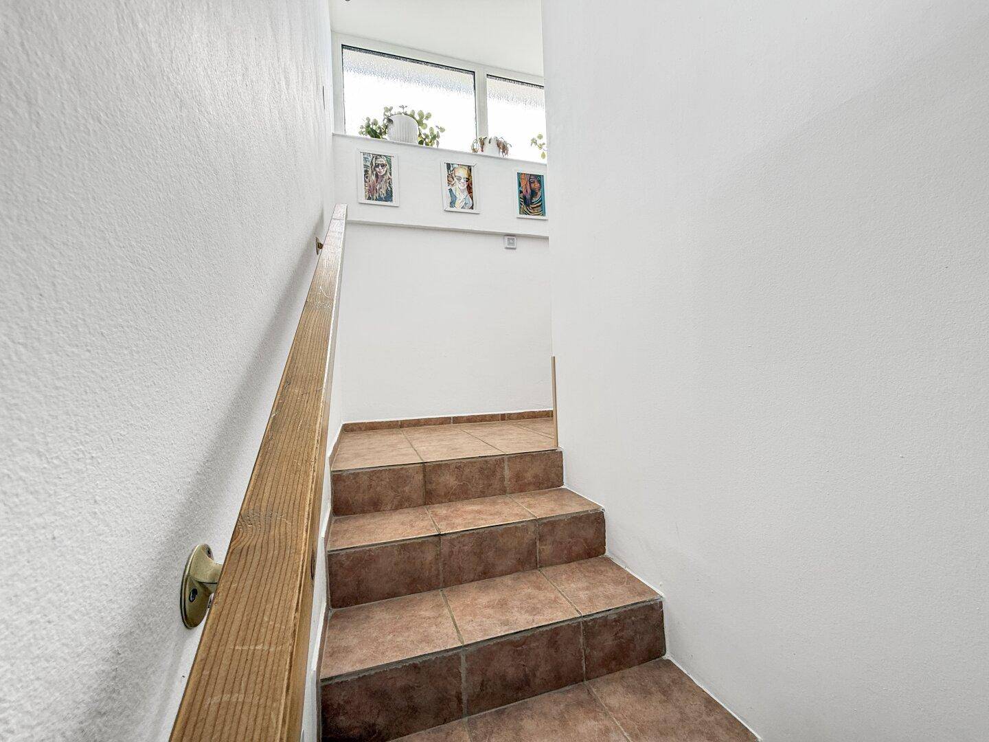 Geflieste Treppe mit Holzgeländer und Fenstern, die natürliches Licht hereinlassen.