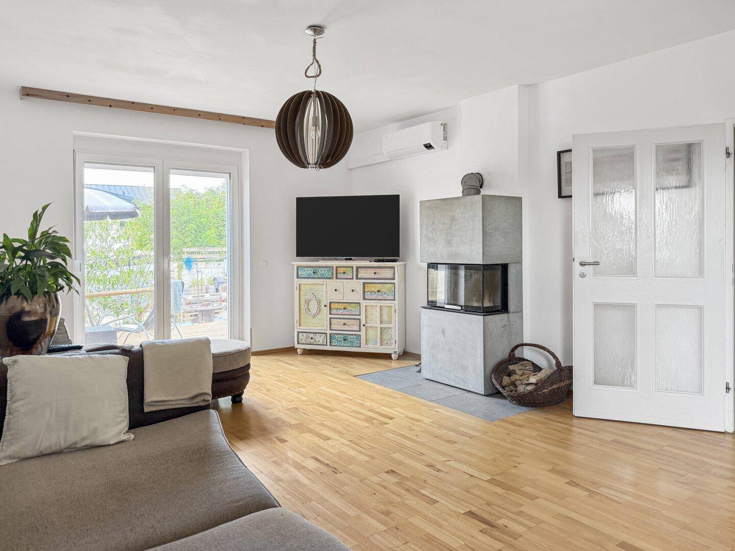 Gemütliches Wohnzimmer mit Kamin, Fernseher und Zugang zu einem Außenbereich.