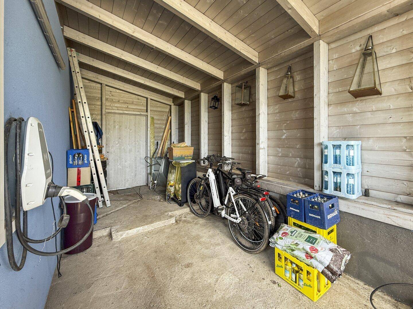 Überdachter Carport mit Ladestation für Elektrofahrzeuge, Fahrrädern und Abstellmöglichkeiten.