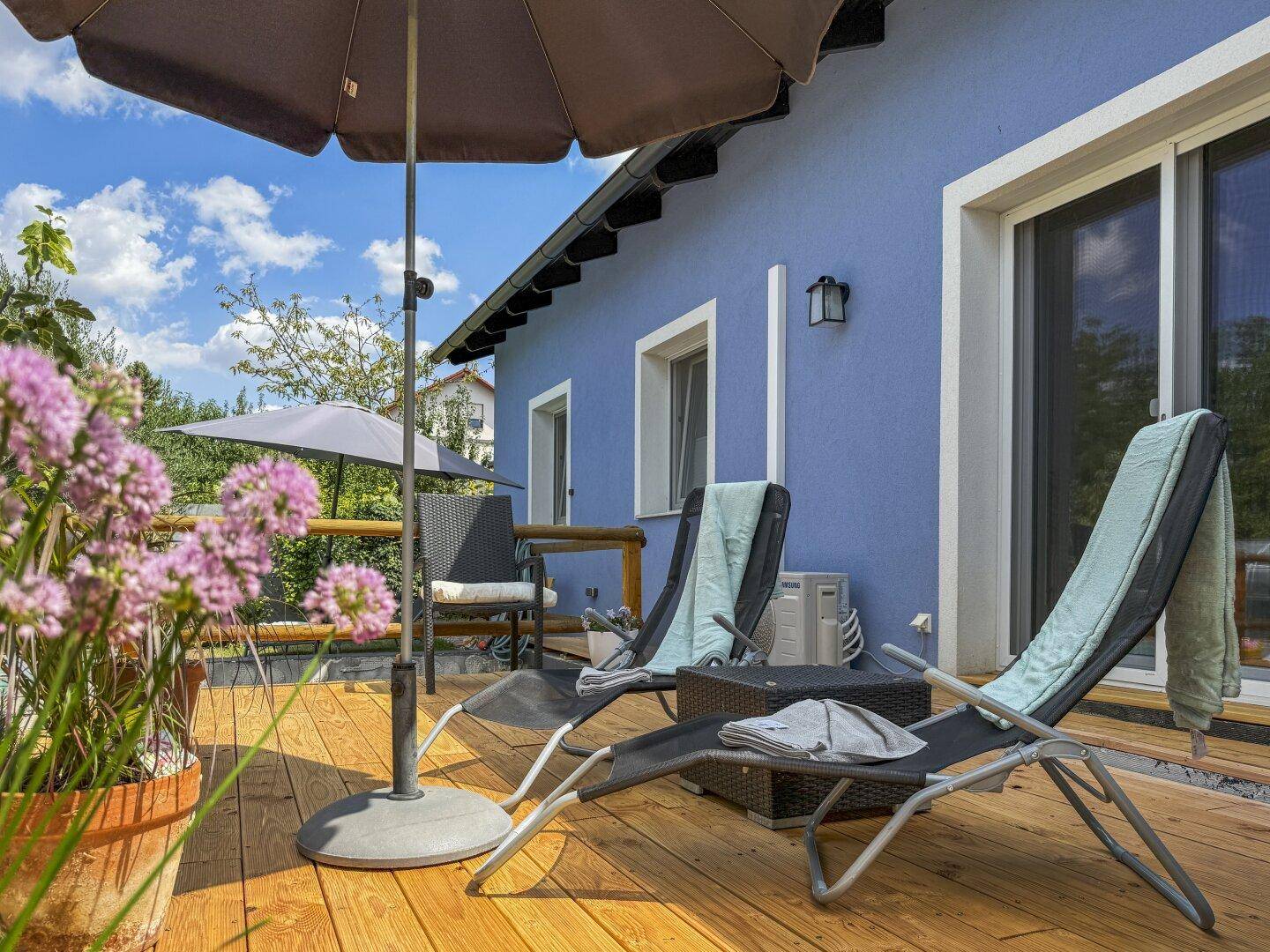 Gemütliche Holzterrasse mit Sonnenliegen und Sonnenschirm, ideal zum Entspannen im Freien.