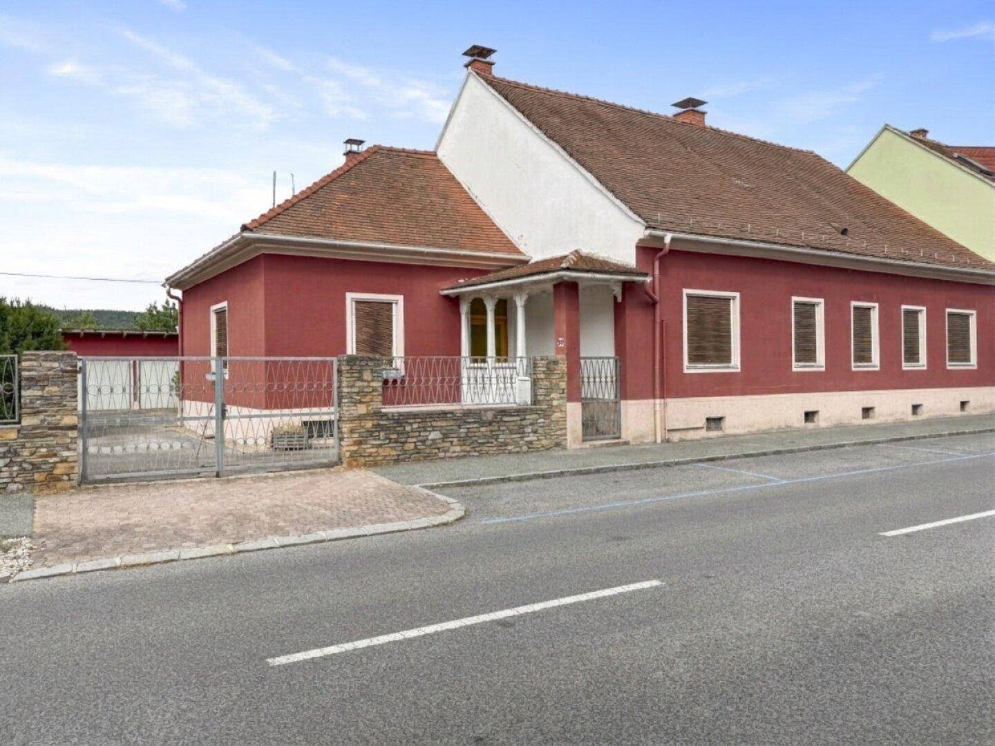 Ansicht des roten Hauses von der Straße mit Veranda und Steinmauer.