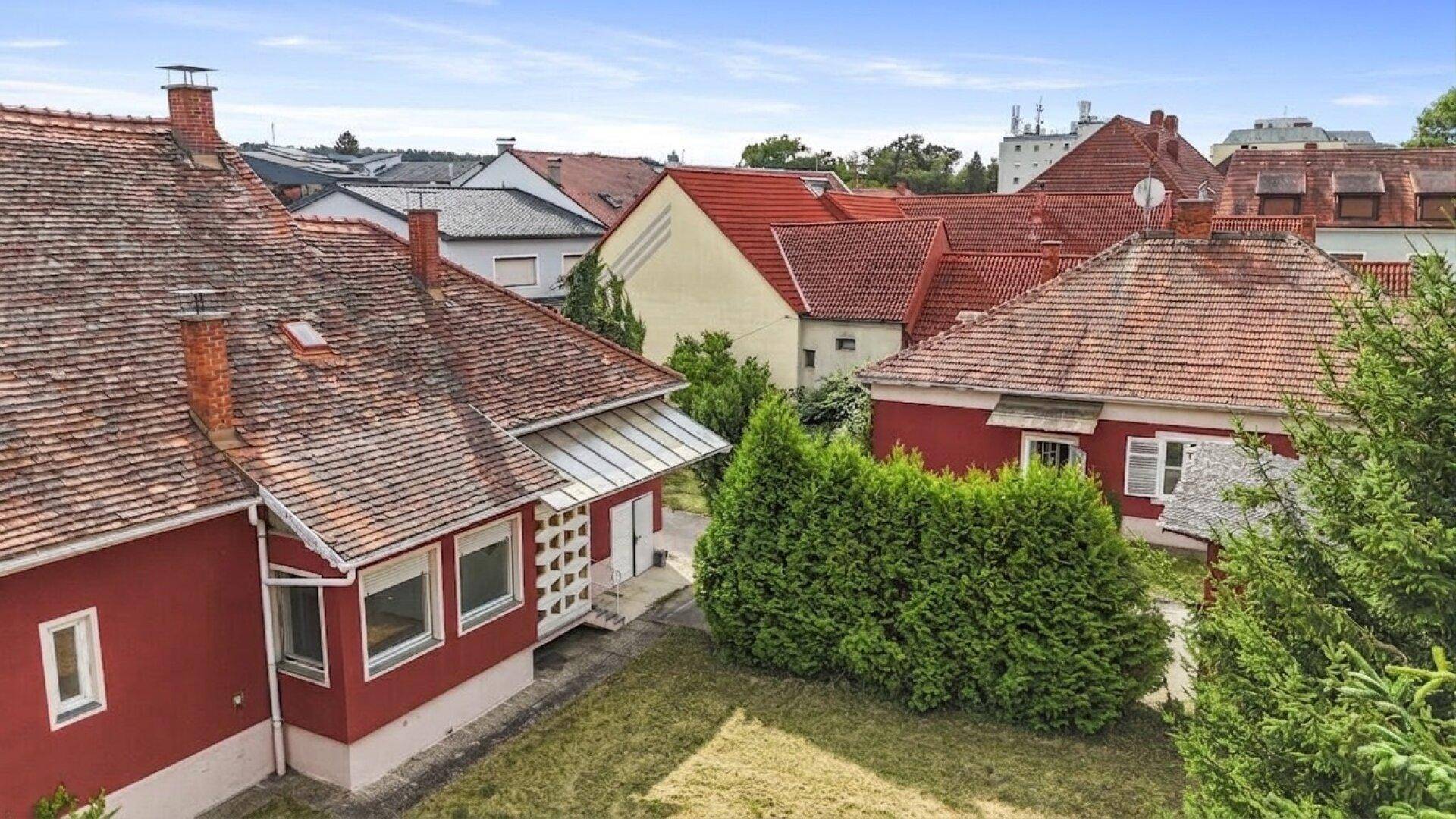 Luftaufnahme des Hauses von hinten mit Garten, Hecke und angrenzenden Gebäuden in der Nachbarschaft.
