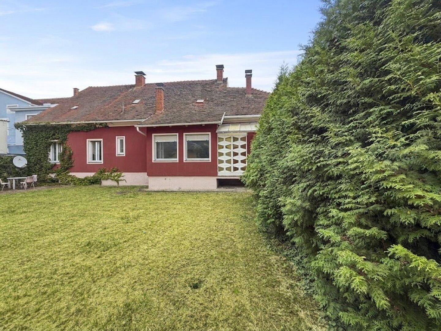 Gepflegter Gartenbereich mit Rasen, hohen Hecken und der roten Fassade des Hauses.
